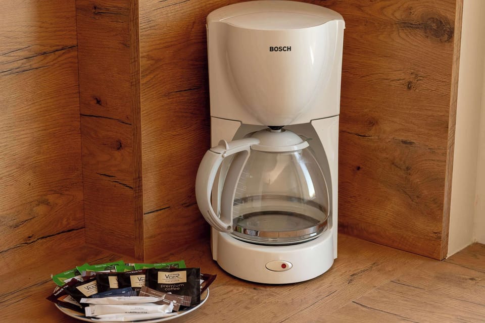 A dedicated close-up shot of the white coffee maker and an open tray of coffee pods reveals the small "BOSCH" logo on the machine, which sits on a wooden surface.