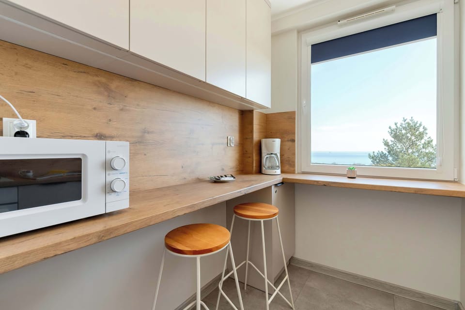 This angle of the kitchen shows the breakfast bar area, with two modern white and orange bar stools tucked under the extended counter near the window. A microwave and other kitchen items are further down the line.