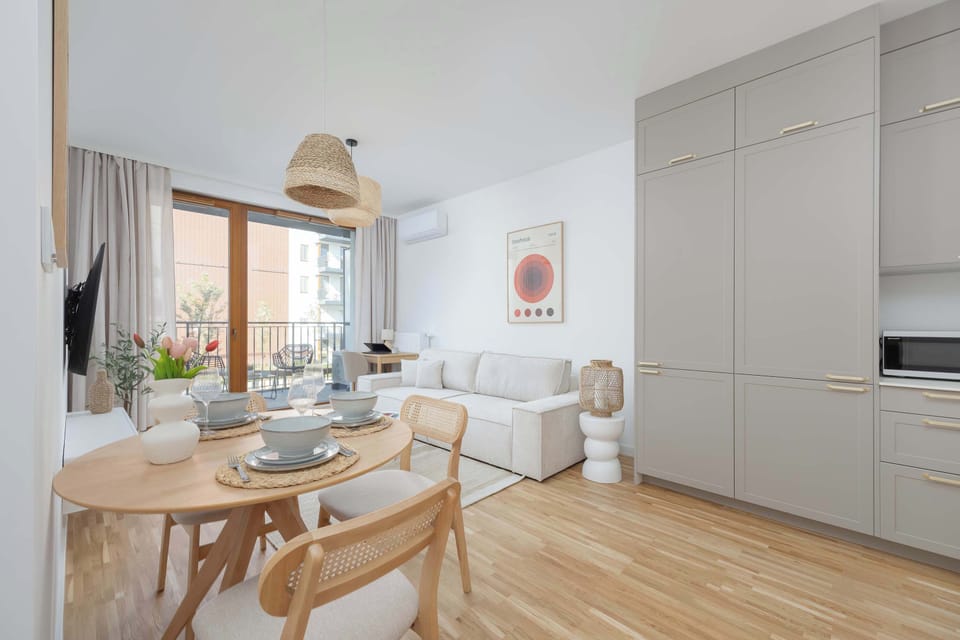 Dining area next to large windows, connected to a bright kitchenette space.