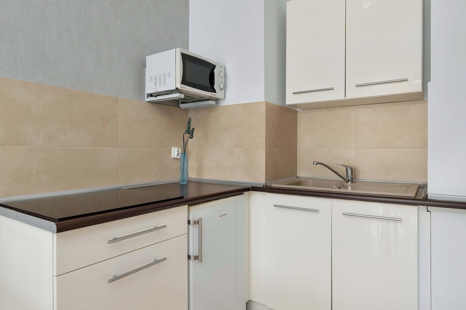 This perspective of the kitchenette highlights the white cabinetry and the contrasting dark countertops. A small white refrigerator is integrated beneath the counter for a space-saving design.