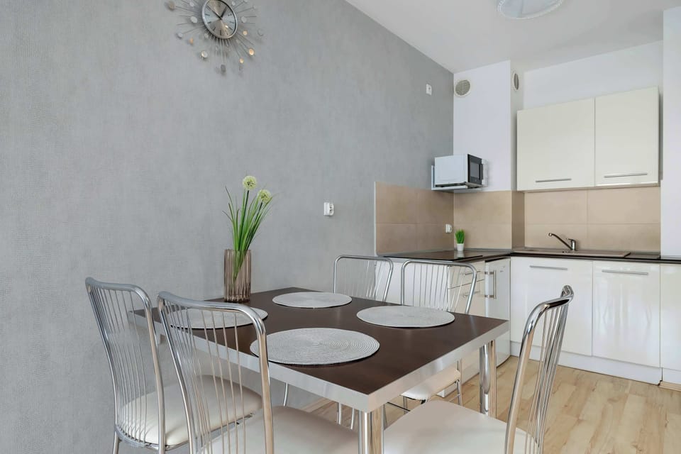 The dining area features a dark wood table with four chrome-legged chairs. It is positioned near the kitchenette, creating a functional flow for dining and meal preparation.