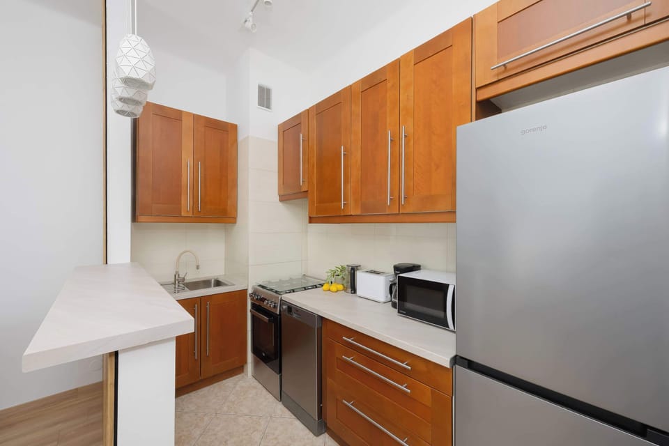A narrow kitchenette with wooden cabinets, light countertops, and modern appliances. The layout is efficient, offering everything needed for cooking in a compact and tidy arrangement.