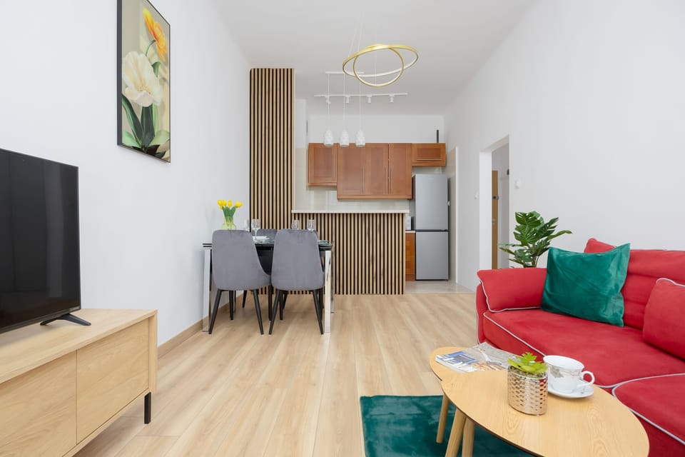 A combined living and dining area where a red couch stands out against a neutral background. A TV and minimalist furniture complete the setup, making it suitable for both relaxing and everyday living.