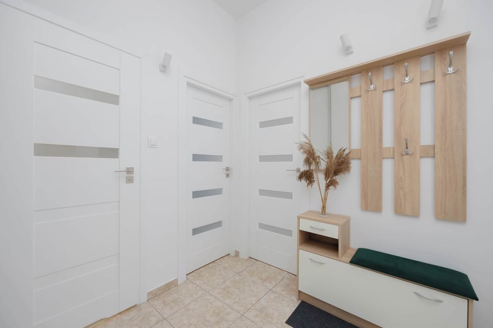 A minimalist corridor with white walls and subtle decorative elements, including wall hooks and a cushioned bench. The space feels open and organized, ideal for storing outerwear and shoes.