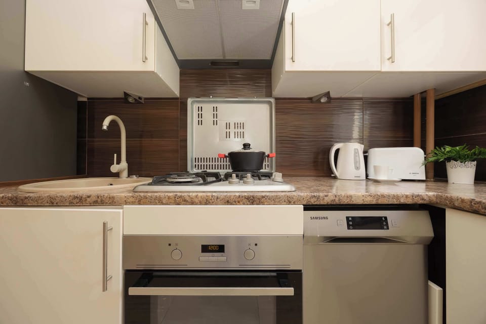 A compact kitchen area features white cabinetry and a built-in oven. The counter is equipped with a small cooktop and essential appliances like a kettle and toaster.