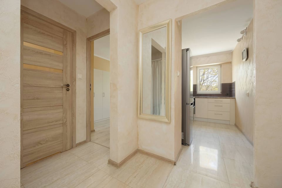 The hallway features several wooden doors and a large mirror that brightens the passage. It serves as a central hub connecting the kitchen and living spaces.