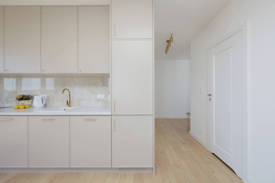 The hallway view shows the entrance to the apartment and the seamless transition into the bright living area. High ceilings and white doors contribute to the overall sense of openness.