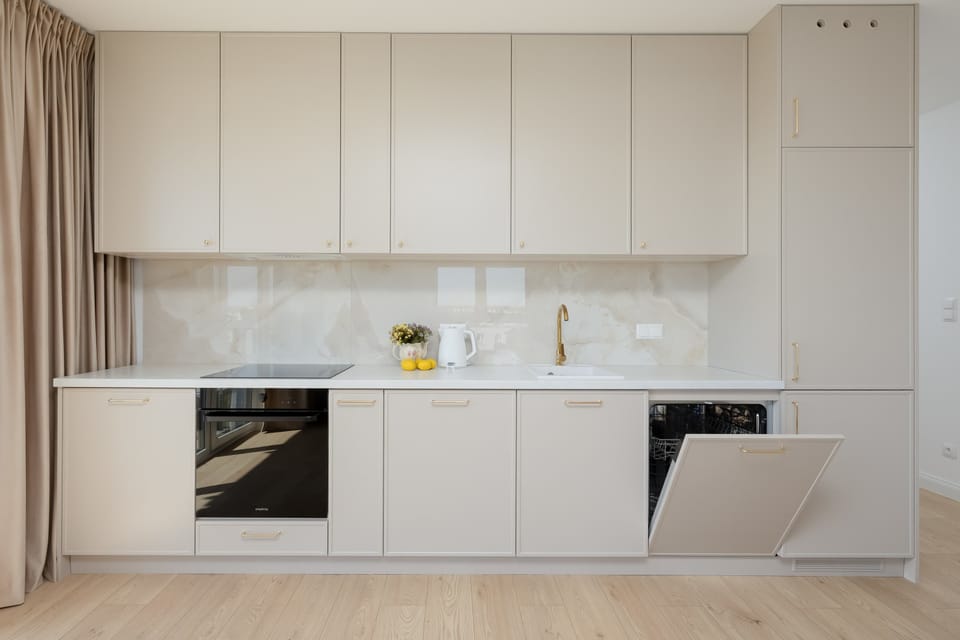 The kitchenette is shown with the dishwasher open, demonstrating the practical and high-end appliances available for guests. Clean lines and white surfaces make the cooking area look pristine and professional.