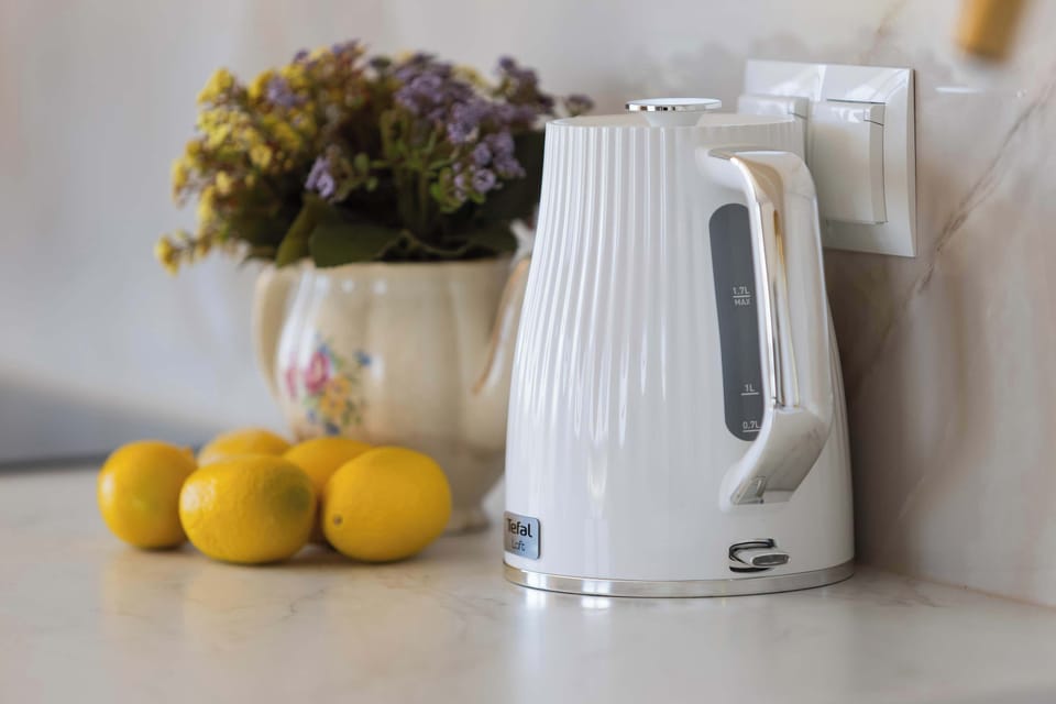 A lifestyle shot features a modern white electric kettle next to fresh lemons, suggesting a homey and welcoming atmosphere. The marble-patterned backsplash adds a layer of luxury to the kitchen workspace.