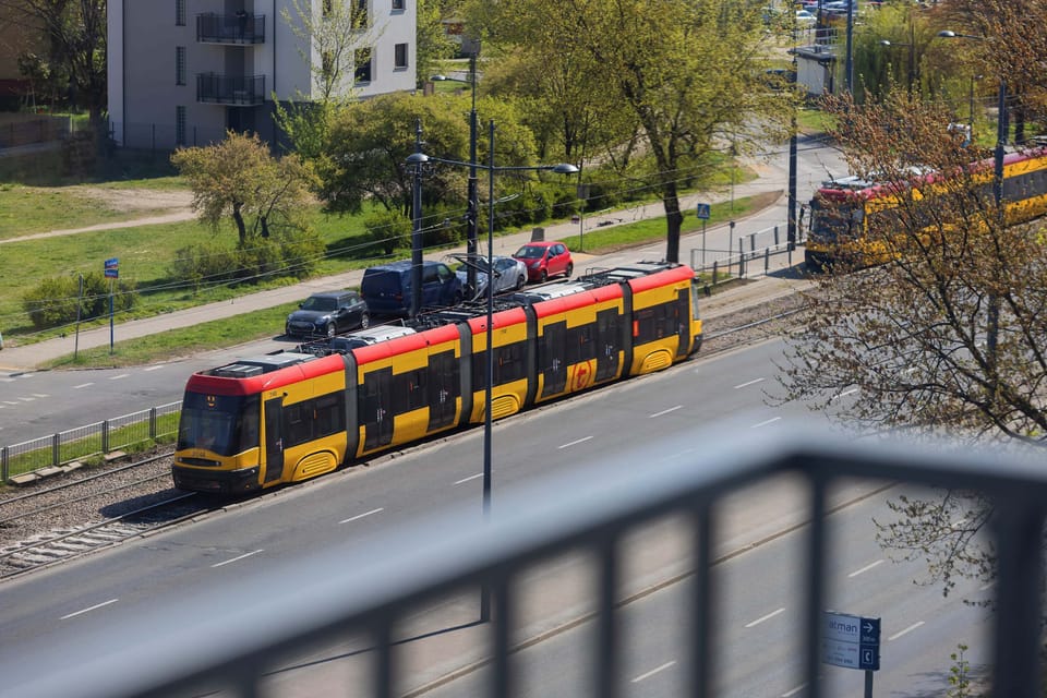 A view from the balcony shows the efficient public transport system, including a modern tram passing through the green corridor. This proximity highlights the excellent connectivity of the location.