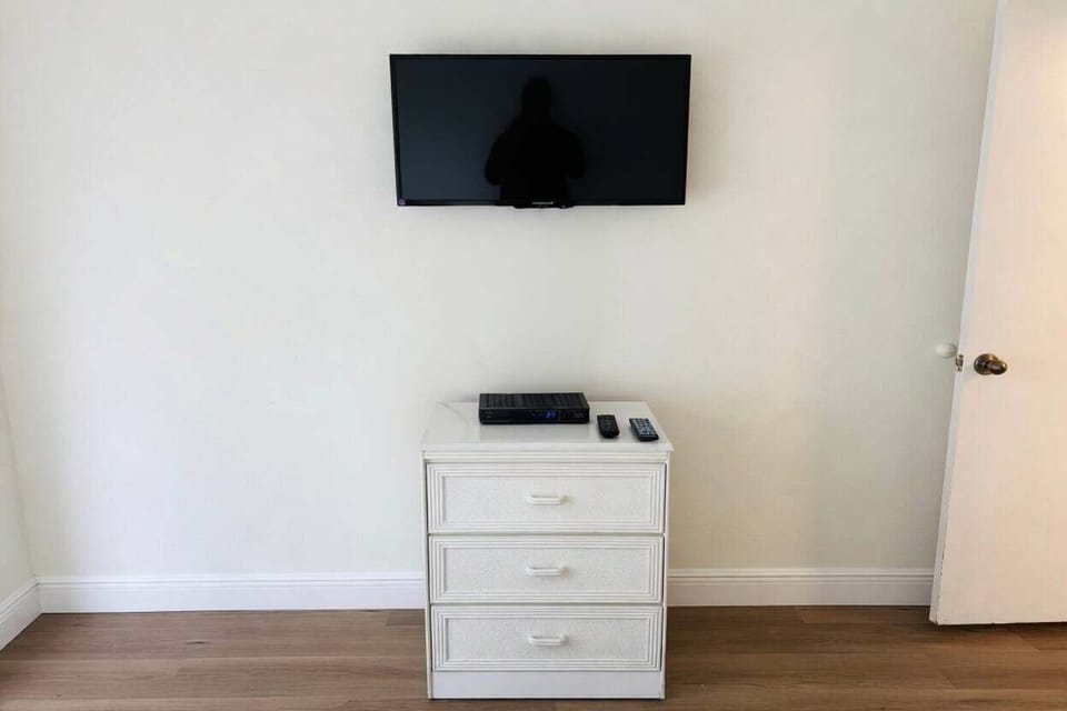 Wall-mounted TV conveniently placed above a white 3-drawer dresser. Perfect for watching movies or shows from the comfort of the bedroom.