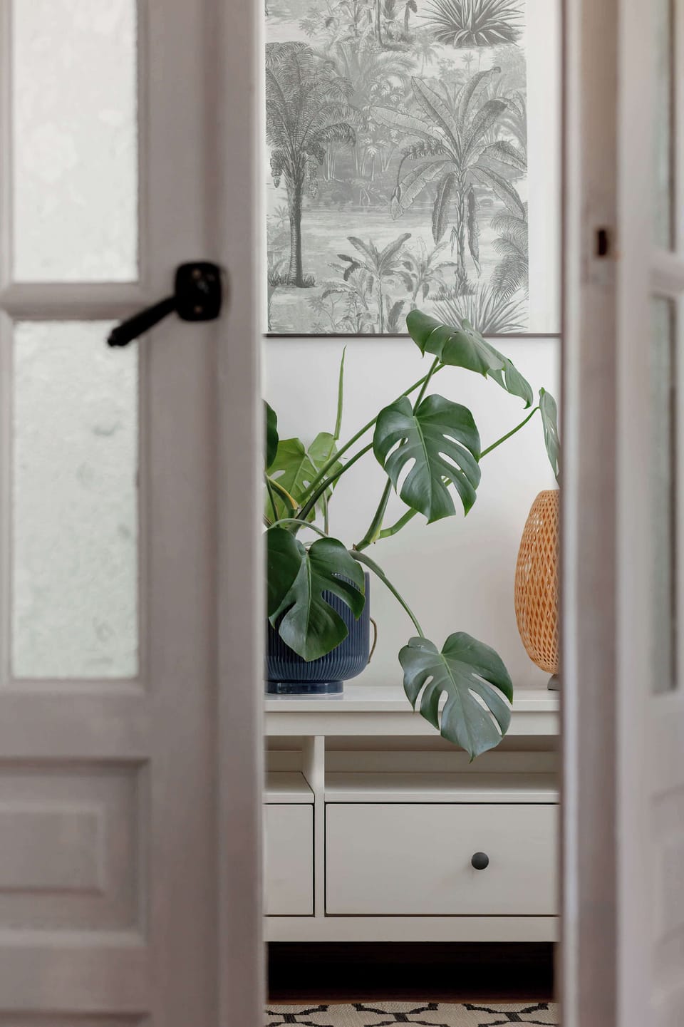 A narrow view through a doorway toward a window with a potted plant placed on the sill.