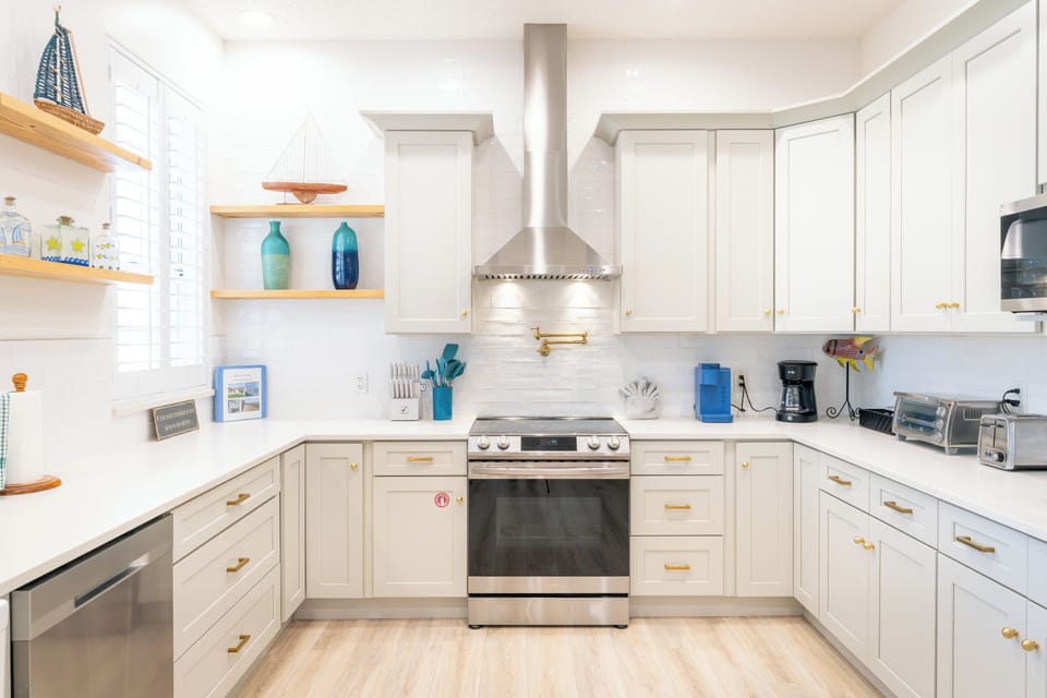 Modern kitchen with stainless steel range, chef's hood, quartz countertops, and gold hardware — fully equipped Palm Coast, FL vacation rental kitchen.