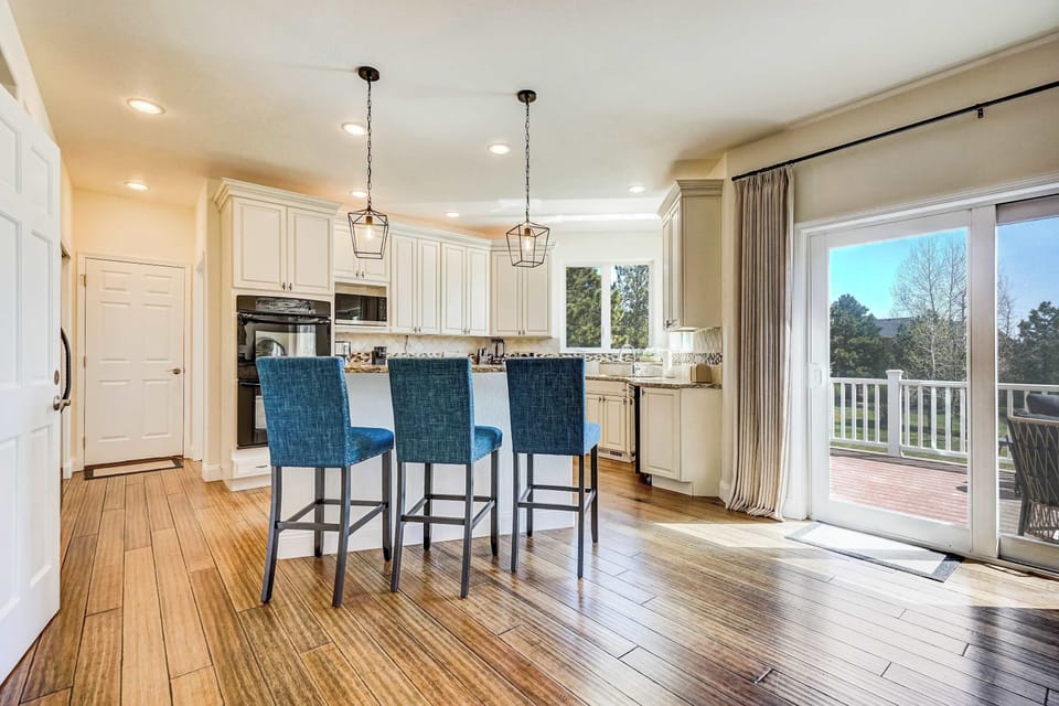 Navy blue island seating adds a bold accent against the white cabinetry and warm floors, while the glass doors to the deck keep the kitchen connected to the outdoors and flooded with natural light.