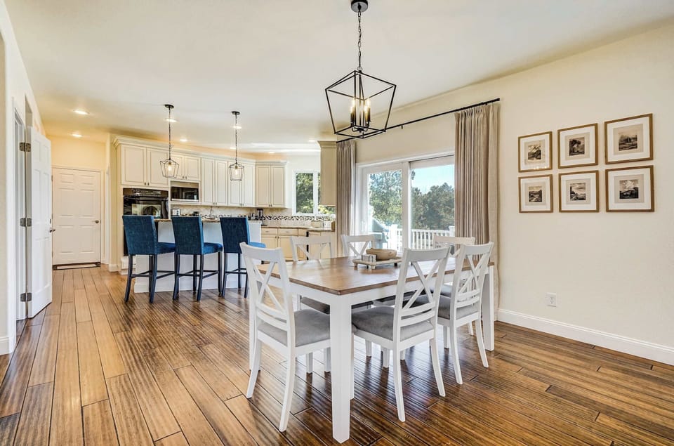 The dining area flows seamlessly into the kitchen, where white cabinetry and navy blue island seating add a crisp contrast against the warm hardwood-style floors and the natural light streaming through the windows.
