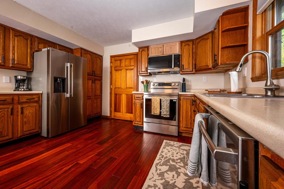 Stainless steel appliances contrast with honey oak cabinets and deep red hardwood floors in the kitchen.