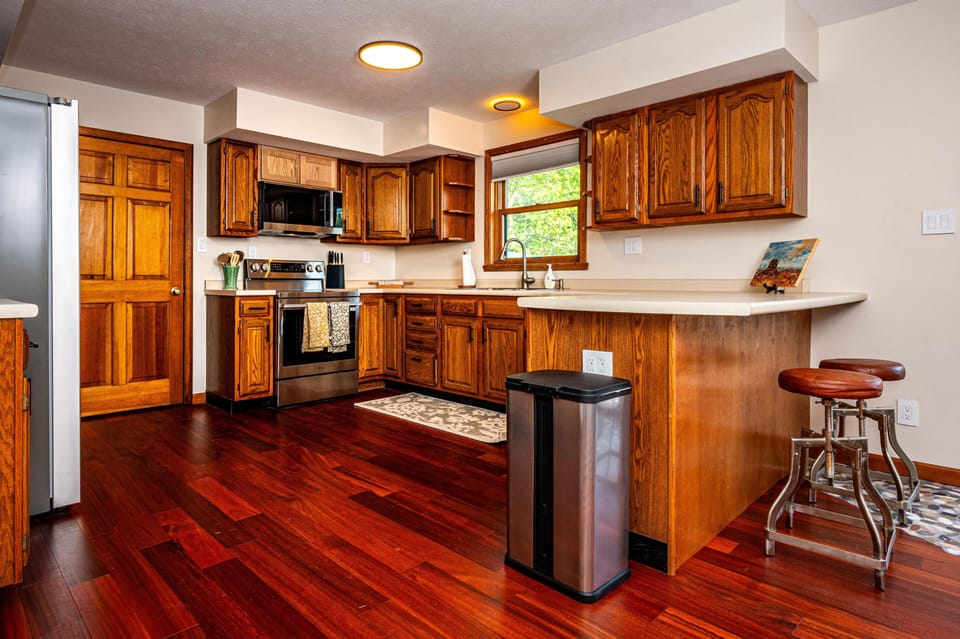 Rich hardwood floors and oak cabinetry frame the kitchen, with a stainless steel stove and window over the sink.