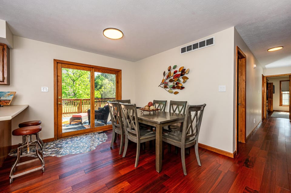 Dining area with dark wood table and six chairs, sliding glass doors opening to a deck with outdoor seating.