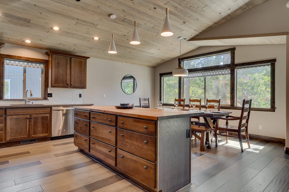 Open kitchen & dining space w/ island seating, rustic finishes & forest views throughout