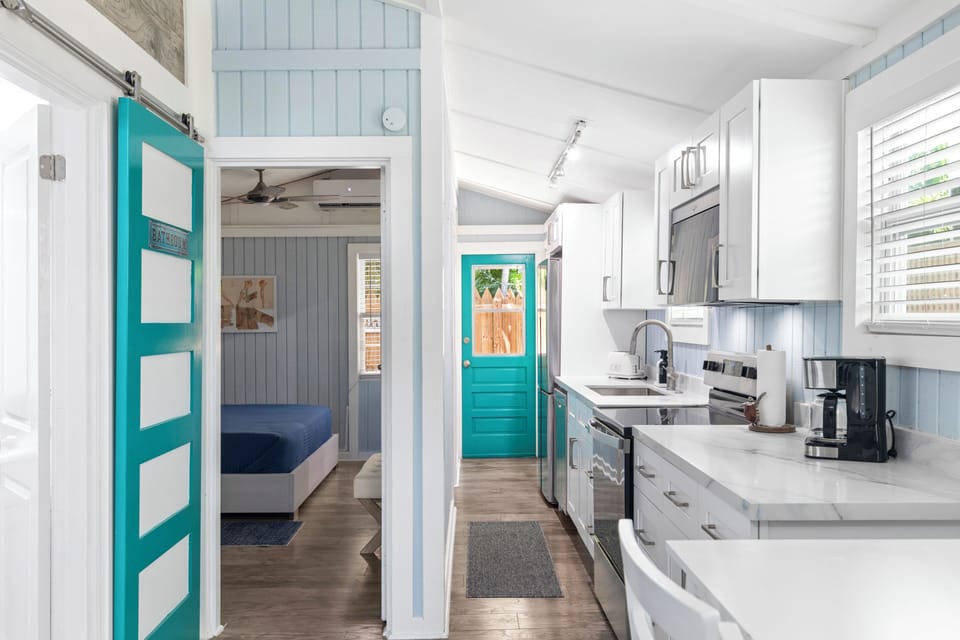 Narrow hallway view looking through the kitchen toward a teal door.
