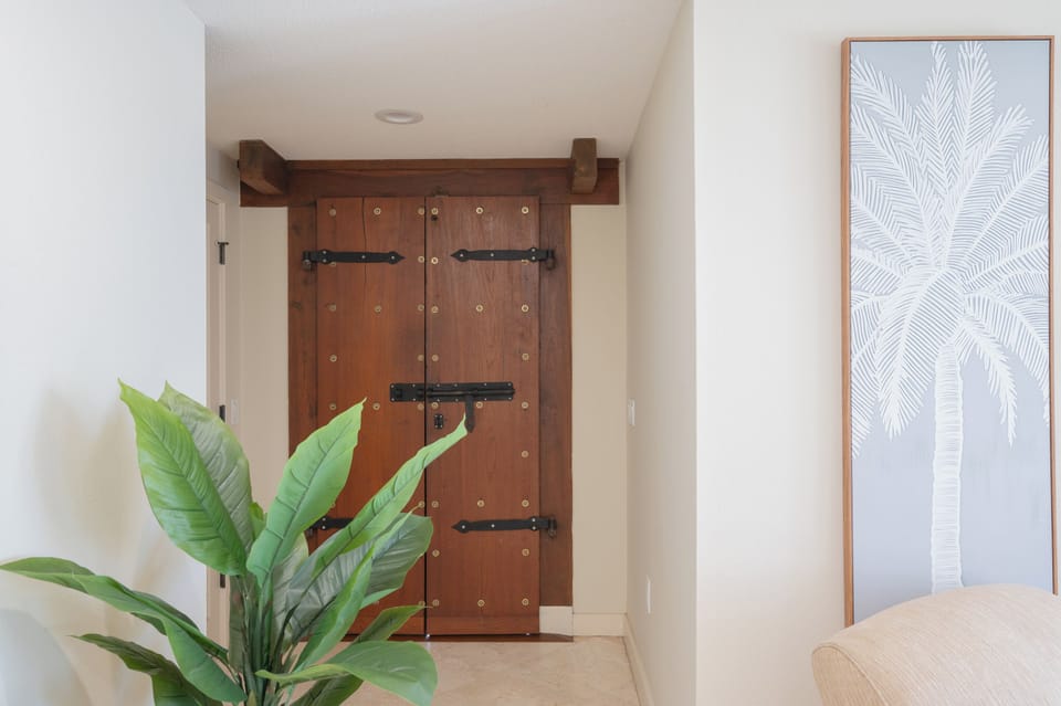 Relax in your serene retreat featuring rustic wooden doors and tropical palm artwork that create a peaceful, resort-inspired atmosphere.