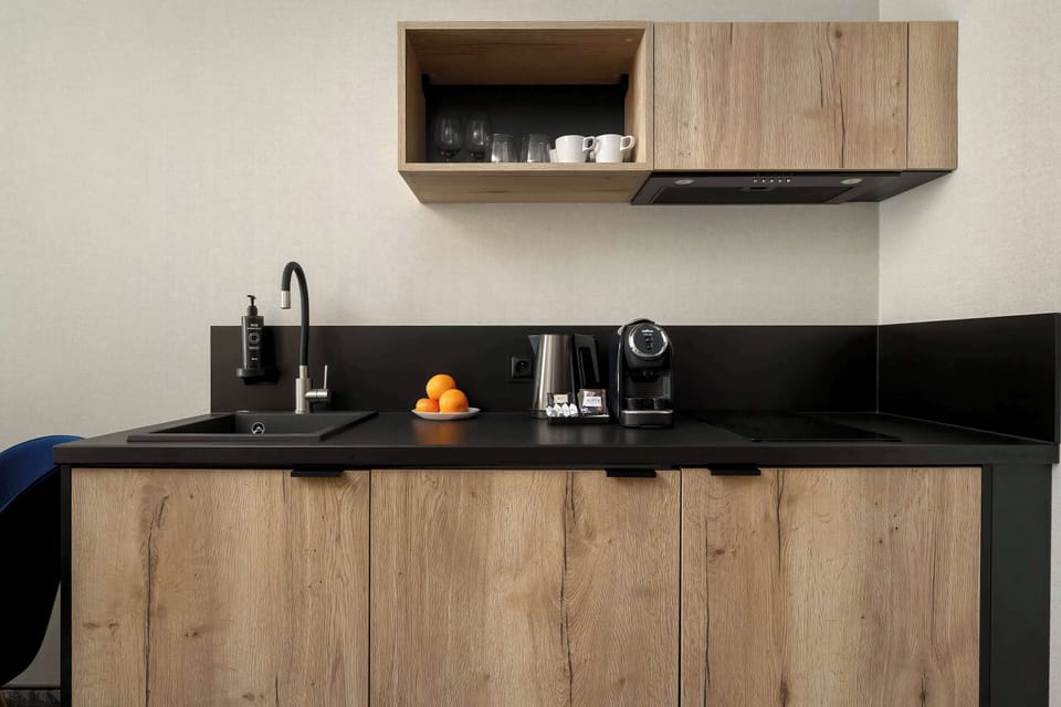 A sleek kitchenette with wooden cabinets and a dark countertop. It includes modern appliances and a tidy workspace.