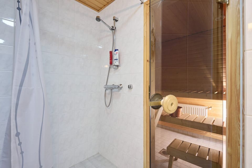 The bathroom features a clean, tiled shower area with easy-to-use temperature controls for a refreshing start to your day. You will also find the entrance to your private sauna right here for a seamless wellness experience.
