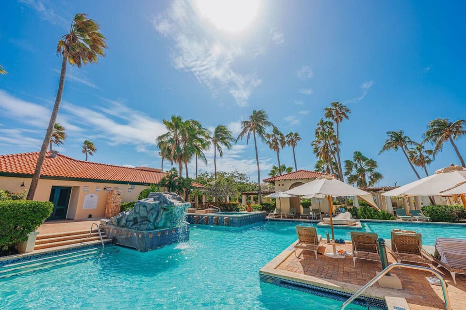 Relax in a tropical oasis with a sparkling pool, palm trees, and sunny lounge areas perfect for a peaceful, resort-style getaway.