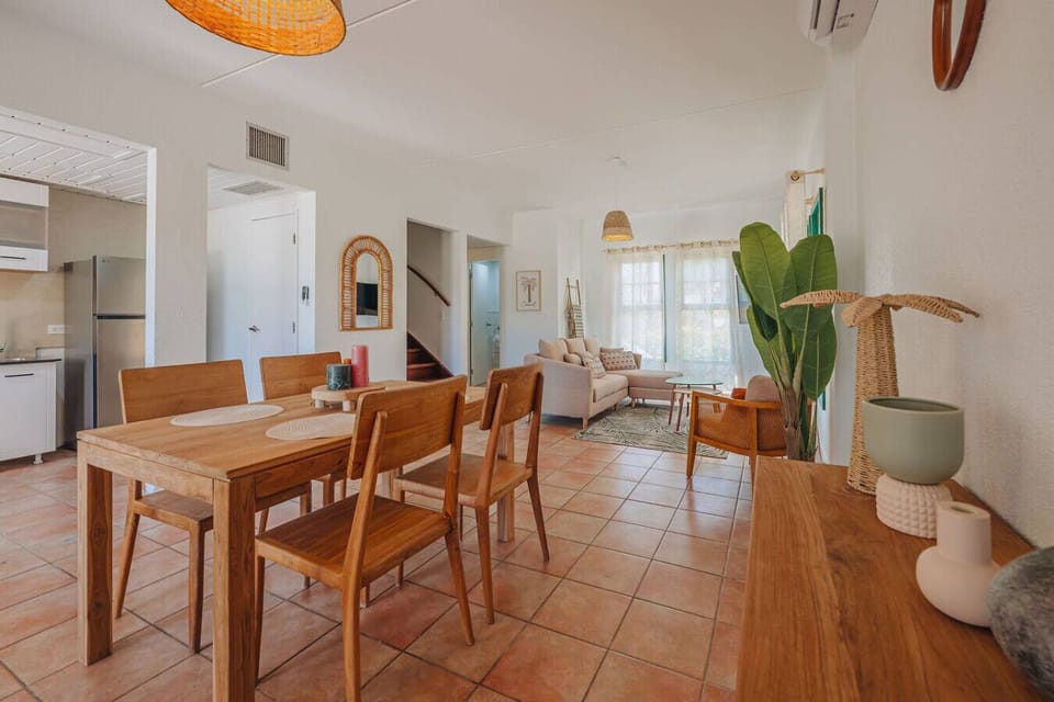 Bright open plan dining and living area with rustic wood furniture, terracotta floors, and natural light perfect for relaxing stays and cozy gatherings.