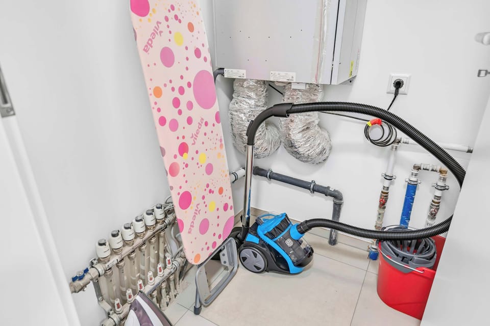 Functional utility area with washing machine, ironing board, and cleaning essentials for added convenience during longer stays