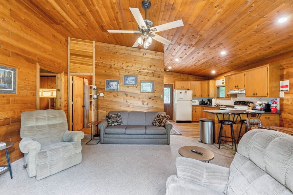 Two Rocking chairs and a gray couch with gray carpet and a ceiling fan.