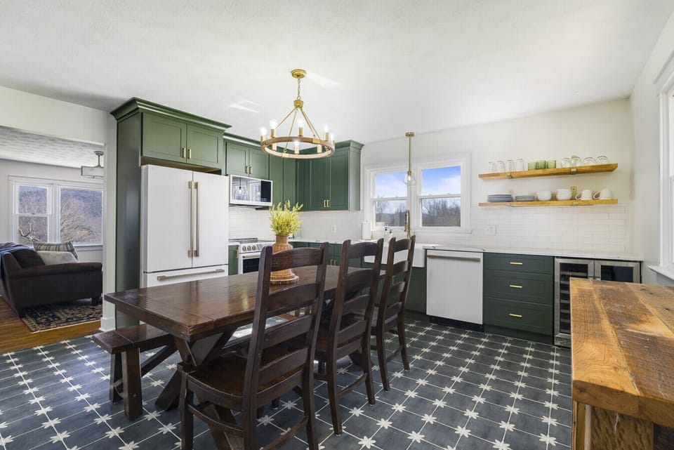Fully equipped kitchen and open-concept dining area featuring designer olive cabinetry, a spacious farmhouse table for group meals, and premium white appliances.