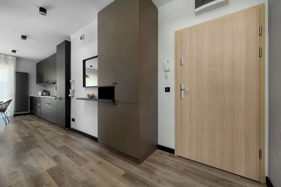 The entrance area features a light wood-toned door and built-in storage solutions. The hallway leads directly into the bright, open-plan living area.