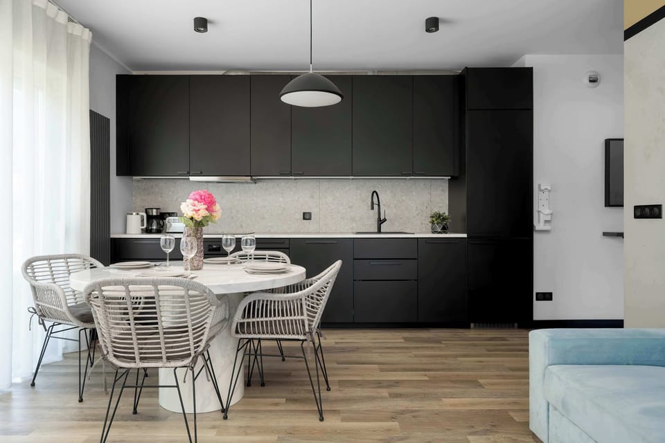 The round white table is surrounded by four stylish chairs under a modern pendant lamp. The black kitchen cabinets provide a dramatic backdrop to the dining space.