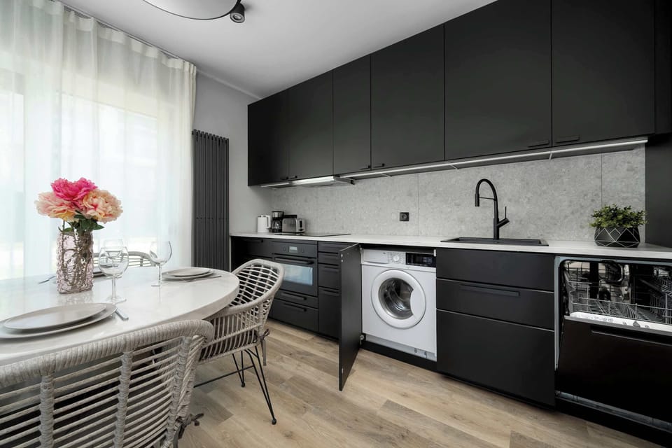 This shot reveals a washing machine hidden within the black kitchen cabinetry, maximizing the use of space. Modern appliances and a clean countertop indicate a high-standard finish.
