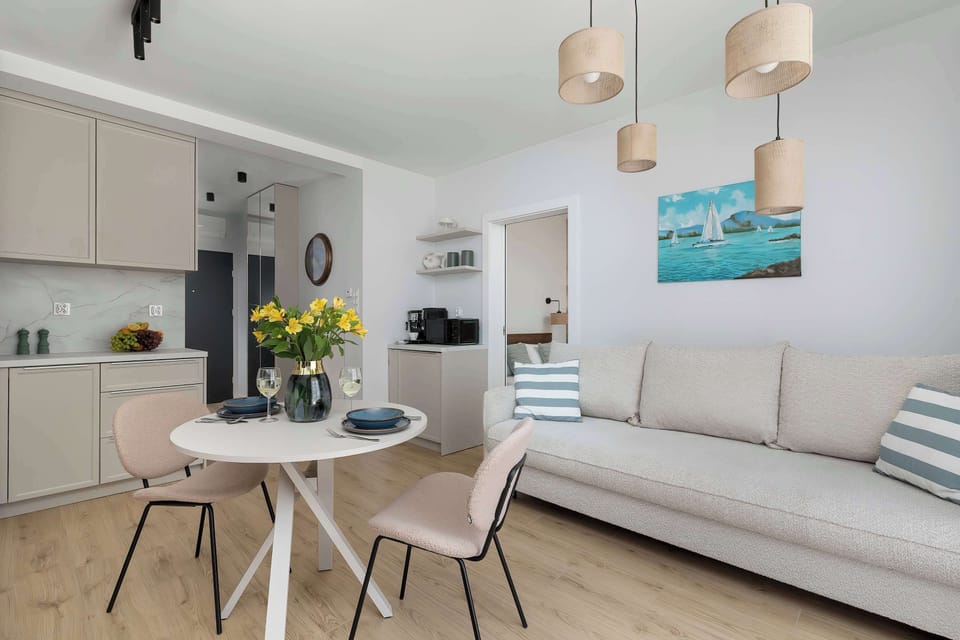 A stylish dining corner with a round table, upholstered chairs, and a view into the kitchen area. Decorative lighting hangs above.