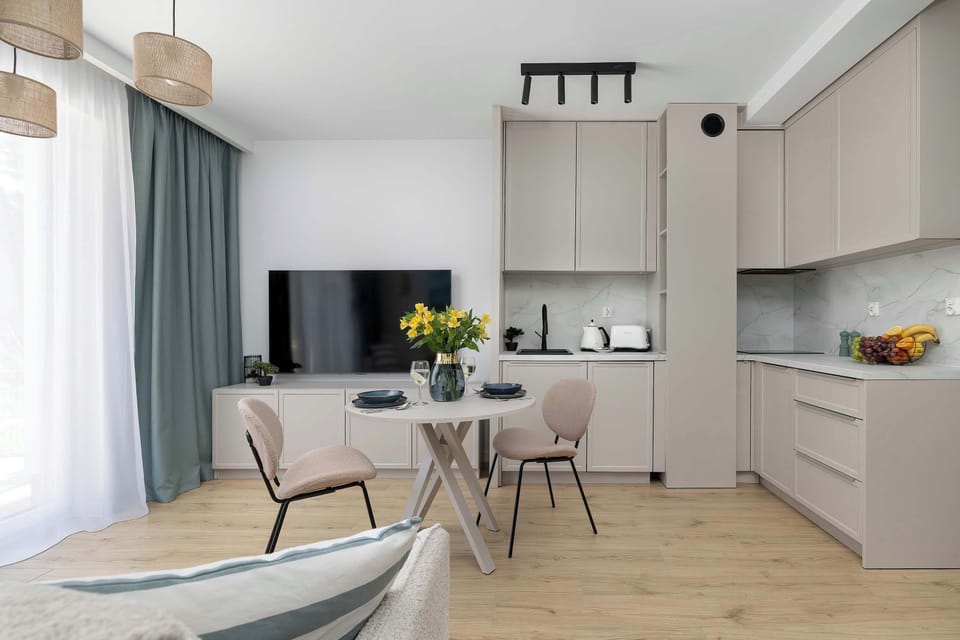 A modern kitchen and lounge space with light cabinetry and a compact seating area. A bouquet on the table adds warmth.
