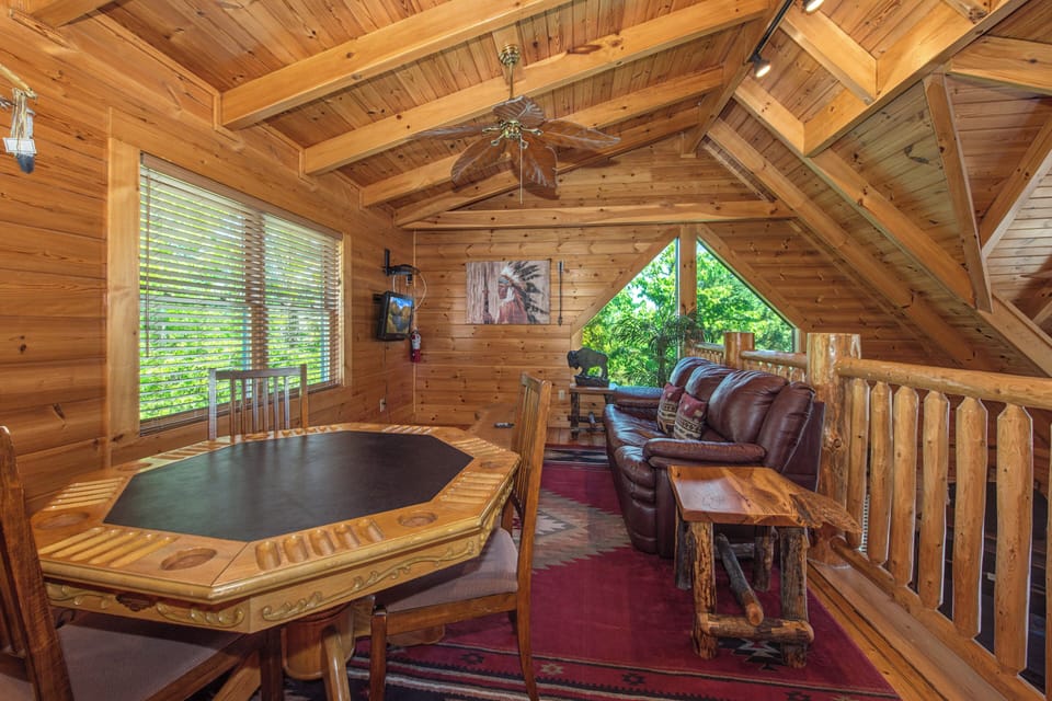 Unwind in your private loft game room with rustic charm, leather seating, and forest views through beautiful windows.