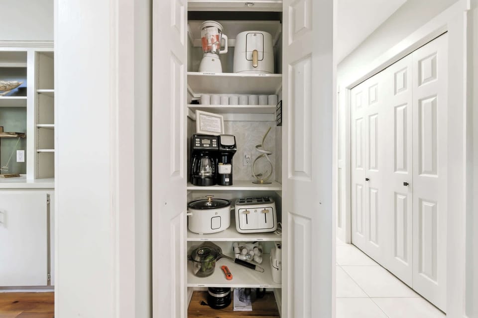 Bright white cabinetry opens to reveal a curated coffee station and modern appliances, perfectly organized for your morning routine. Creamy tones and gold accents create a polished, functional nook that makes vacation breakfast a breeze.