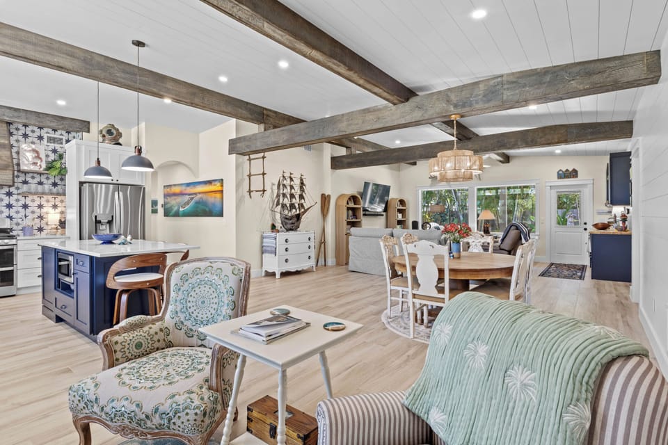 Step into your coastal-inspired open living space where rustic beams meet modern comfort, perfect for gathering around the kitchen island.