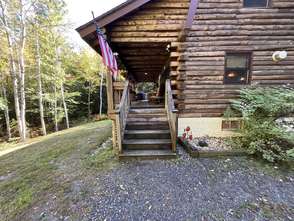 Rustic log cabin entrance with covered porch nestled among towering trees, offering a peaceful retreat.