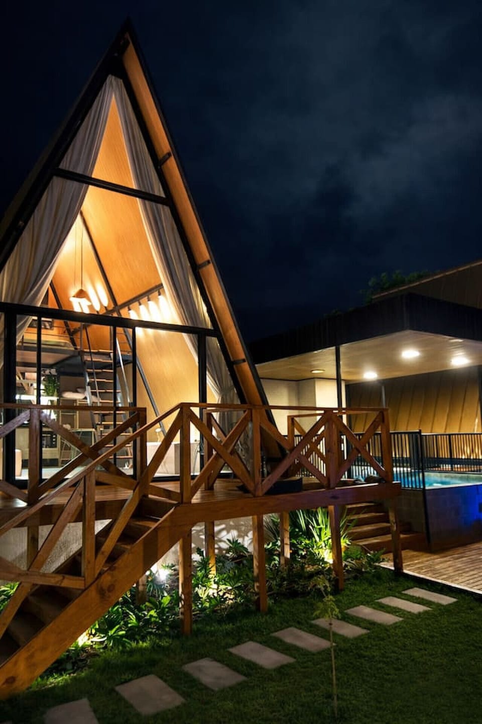 A Cabana Country impressiona pelo pé-direito alto, estrutura em madeira e amplas fachadas envidraçadas que valorizam a iluminação natural durante o dia e criam um cenário aconchegante à noite.  A varanda elevada conecta os ambientes com elegância, enquant