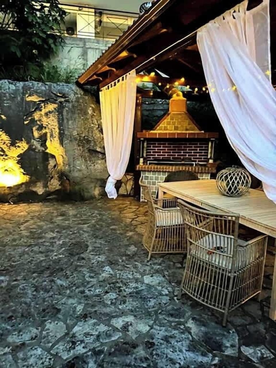 Charming covered outdoor dining area with BBQ and ambient lighting