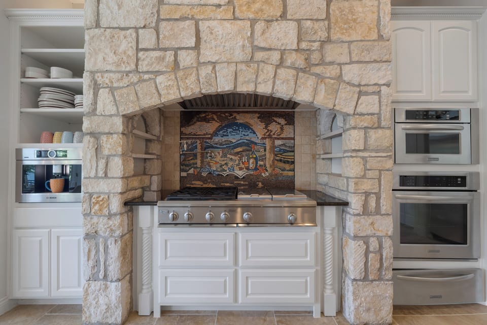 Six burner range under a stone arch with mosaic tile