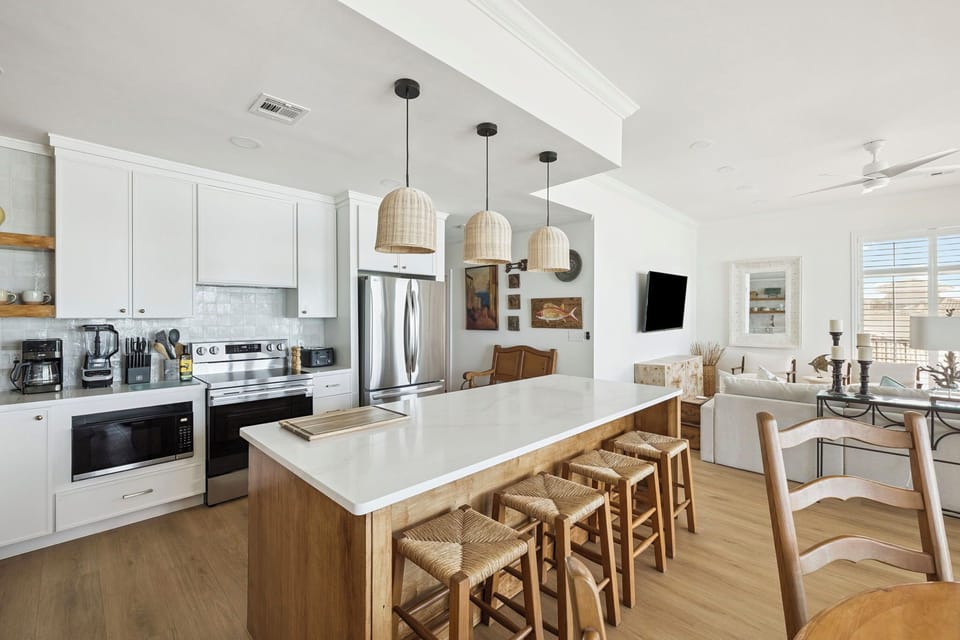 Your open-concept kitchen and living space awaits with modern appliances, warm woven pendant lights, and a spacious island for cooking and gathering together.