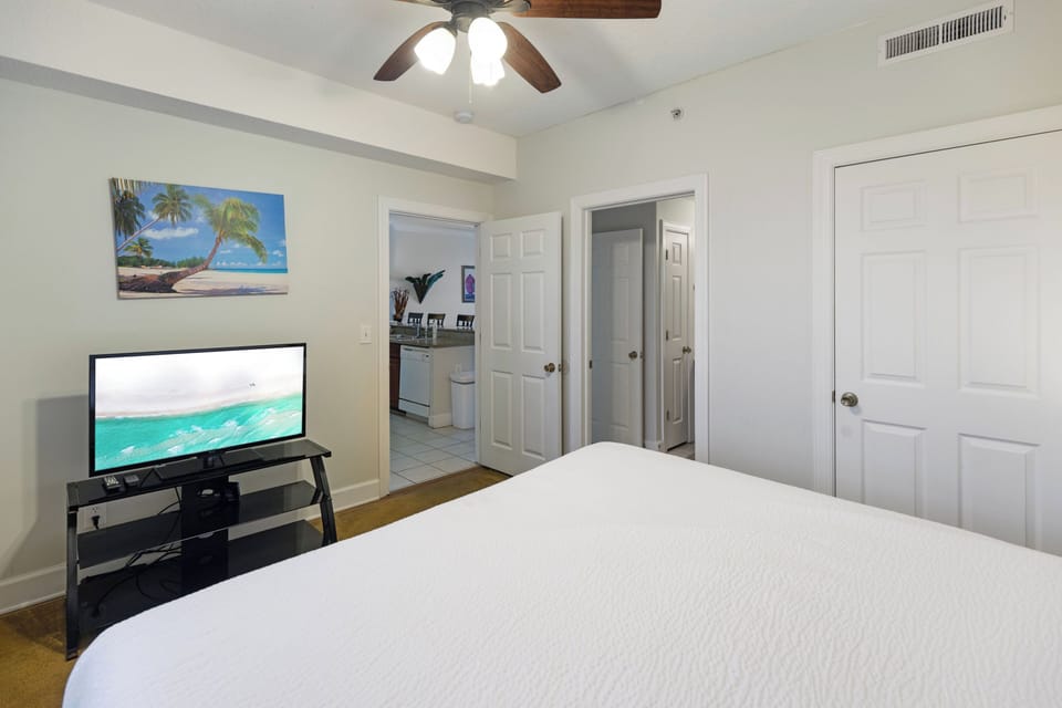 Relax in your coastal-themed bedroom featuring crisp linens, tropical artwork, and modern entertainment center with flat-screen TV.