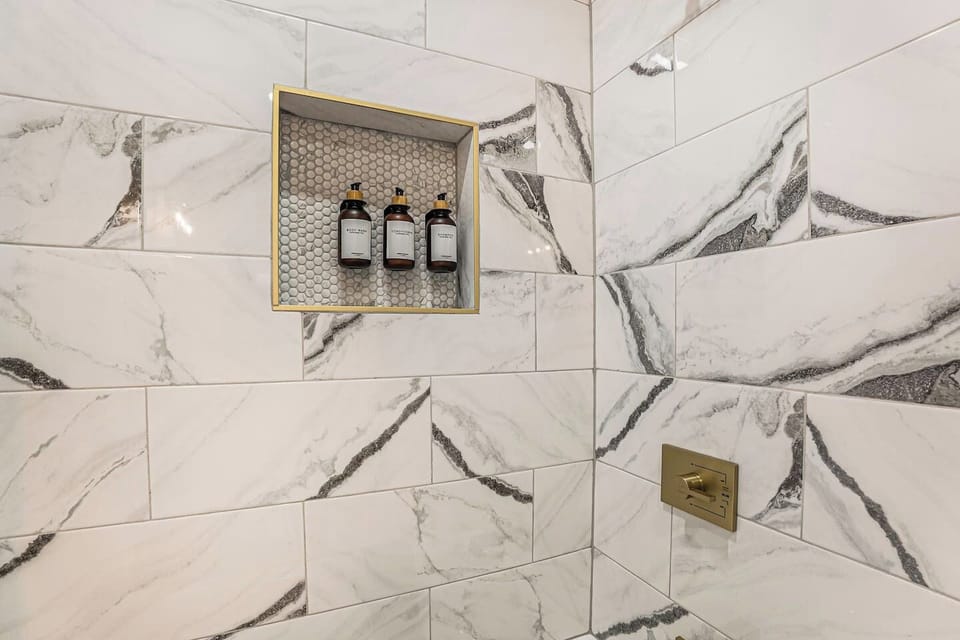 Marble Bath - Newly renovated shower with built-in shampoo, conditioner, and body wash, featuring elegant marble and gold accents.
