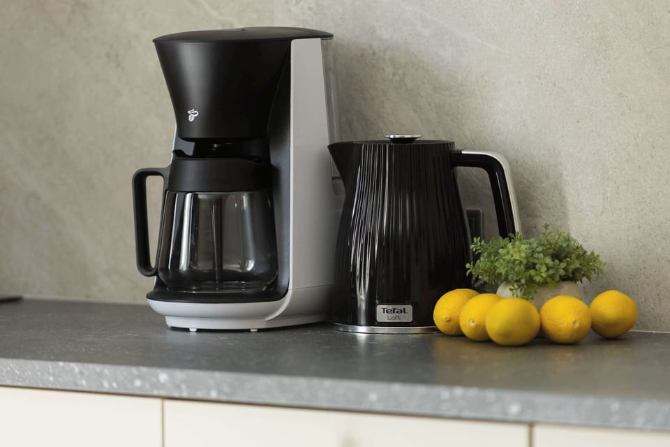 A kitchenette countertop with a coffee maker and a few fresh lemons placed beside it. The setup suggests a convenient space for preparing morning drinks.