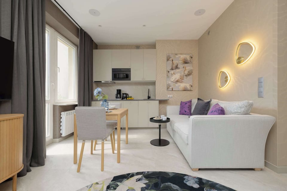 A stylish living and dining area with a small table and chairs next to a comfortable sofa. Decorative wall lighting and soft furnishings create a warm, inviting atmosphere.