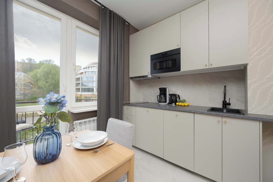 A compact kitchenette with sleek cabinetry and a light countertop. A window nearby adds brightness, while minimal decor keeps the space clean and functional.